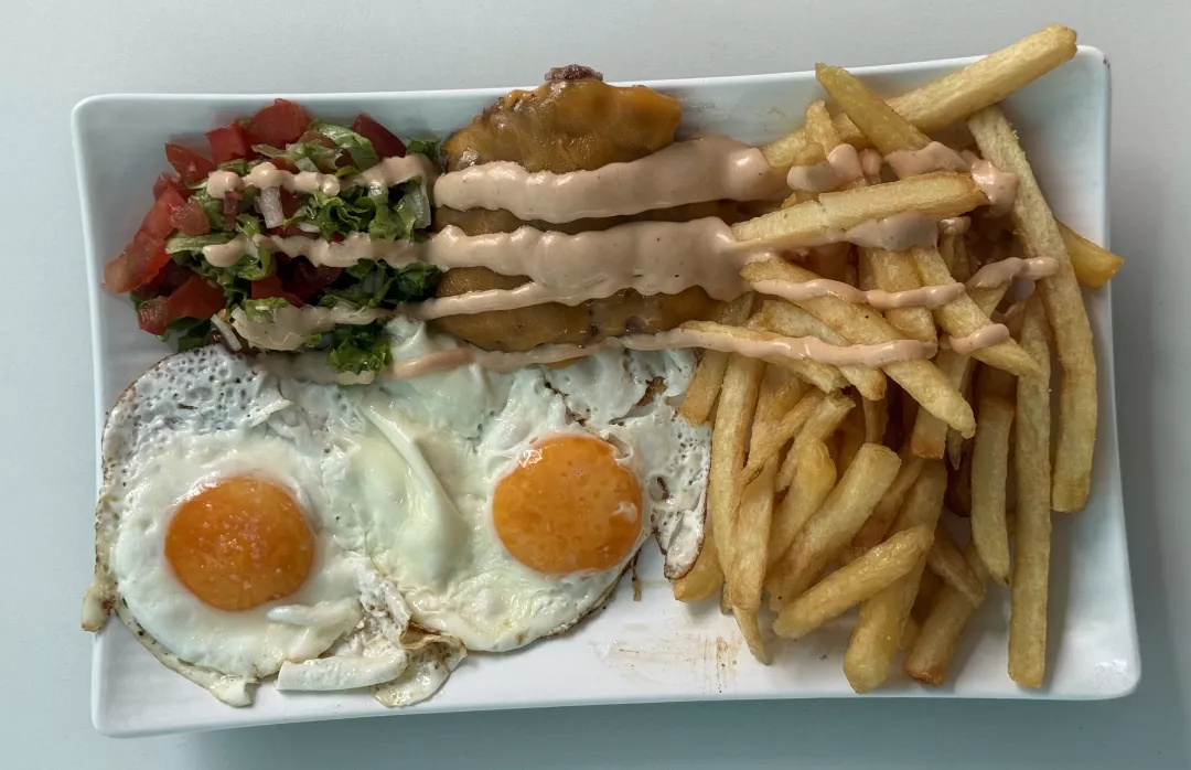 Plato combinado de carne de hamburguesa, papas, huevos y ensalada.